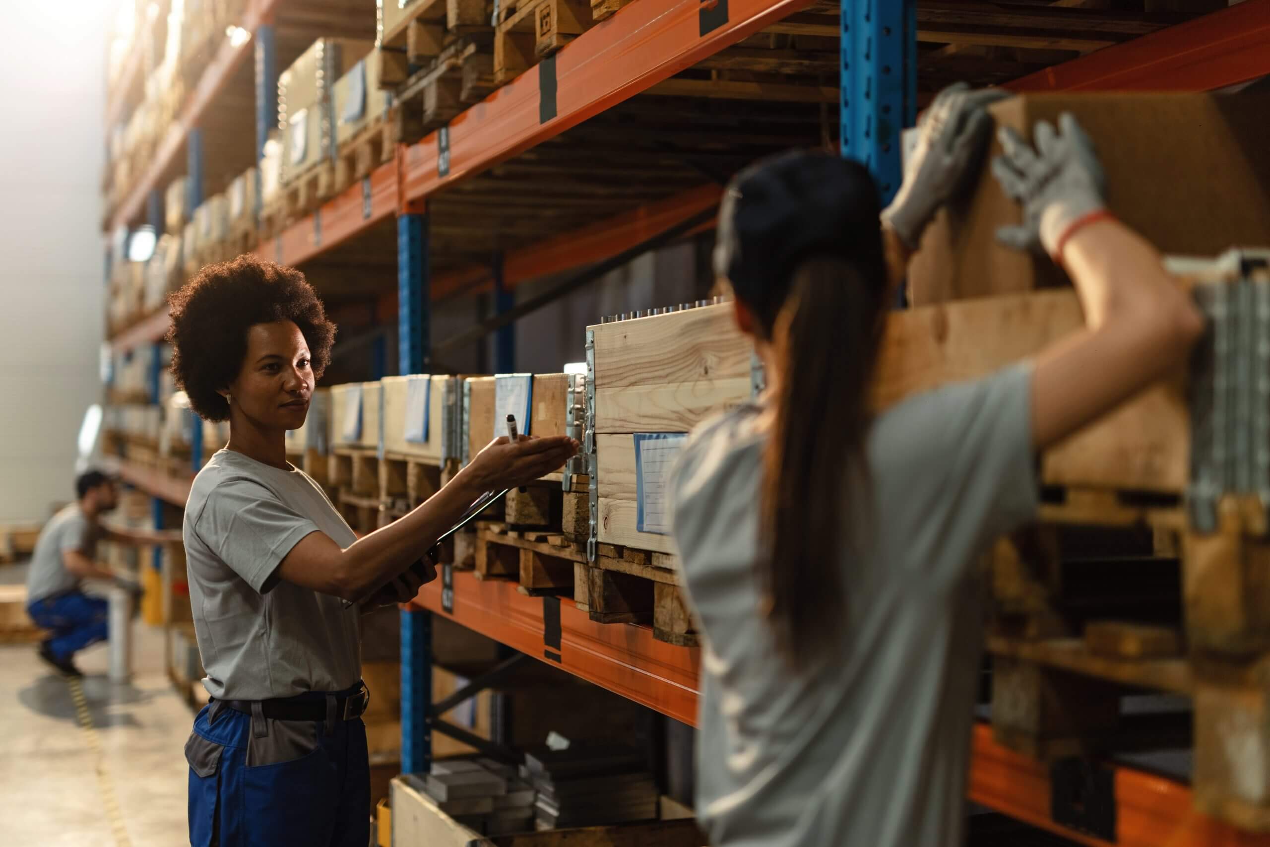 African American worker communicating with her female colleague while preparing shipment in industrial warehouse.